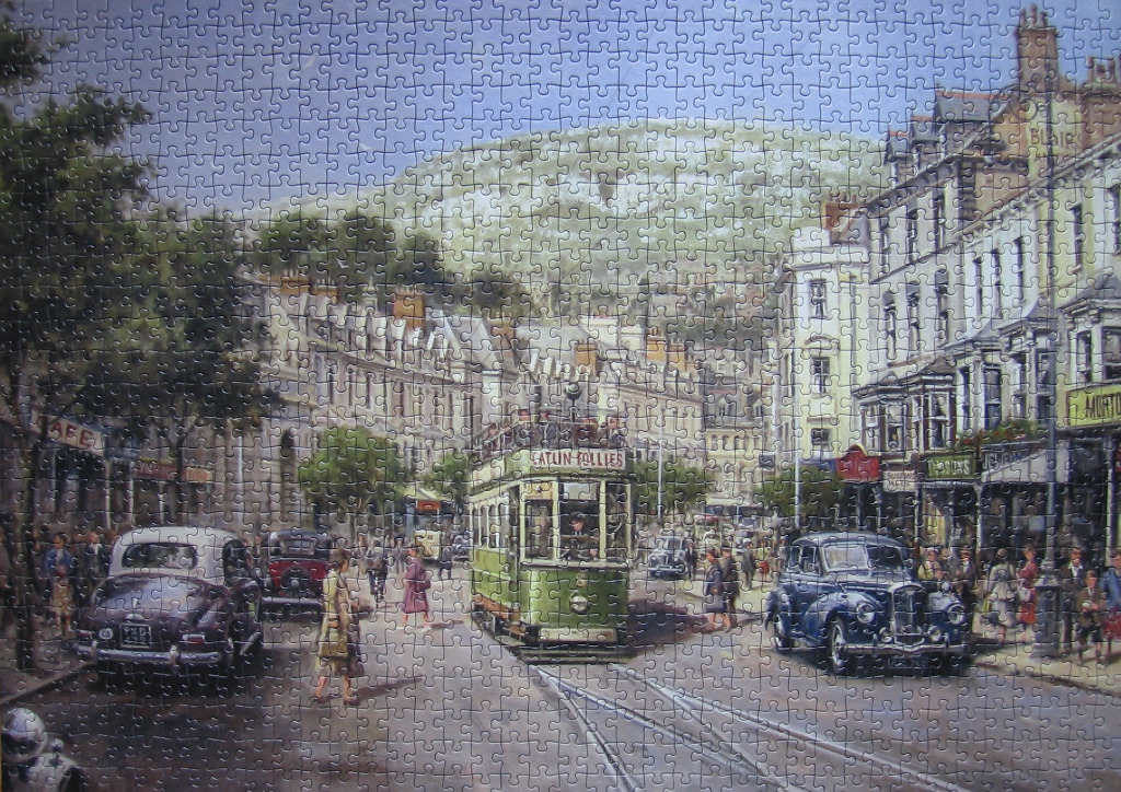 A vintage town street scene with a green tram, classic cars, and pedestrians set against a mountainous backdrop.