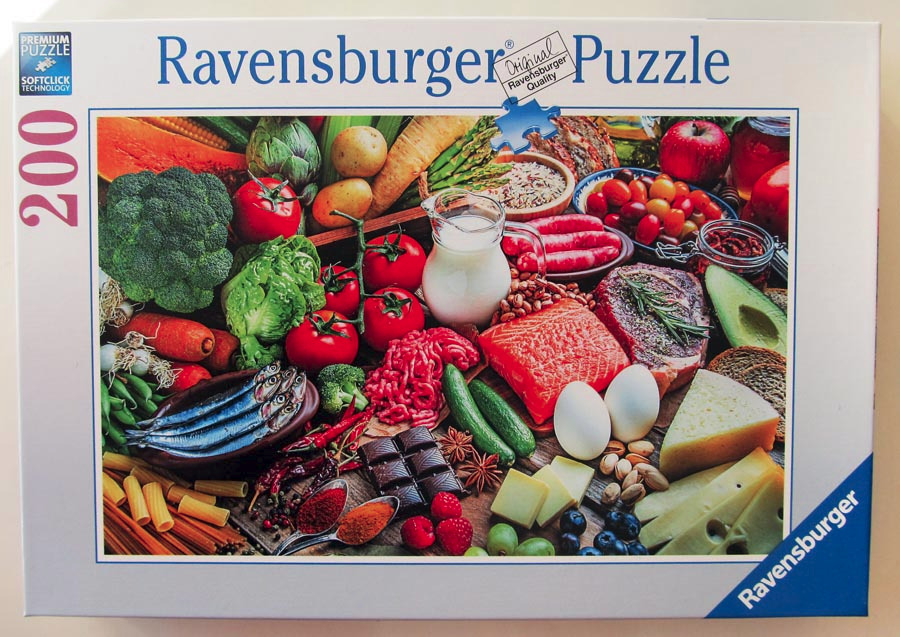 A high-angle, crowded food scene featuring fresh produce, raw meat, fish, dairy, and spices spread across a wooden surface.