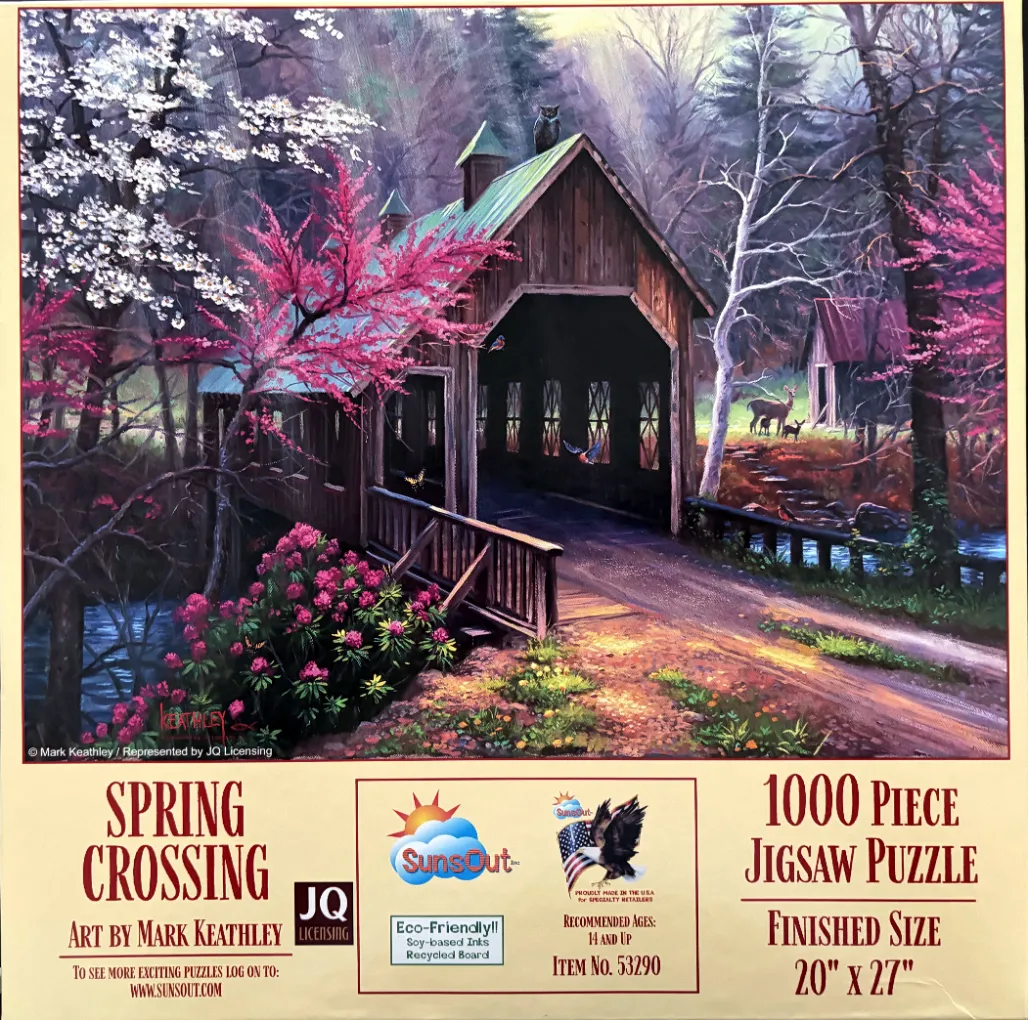 A covered wooden bridge spanning a stream in a spring forest with flowering dogwood and redbud trees.