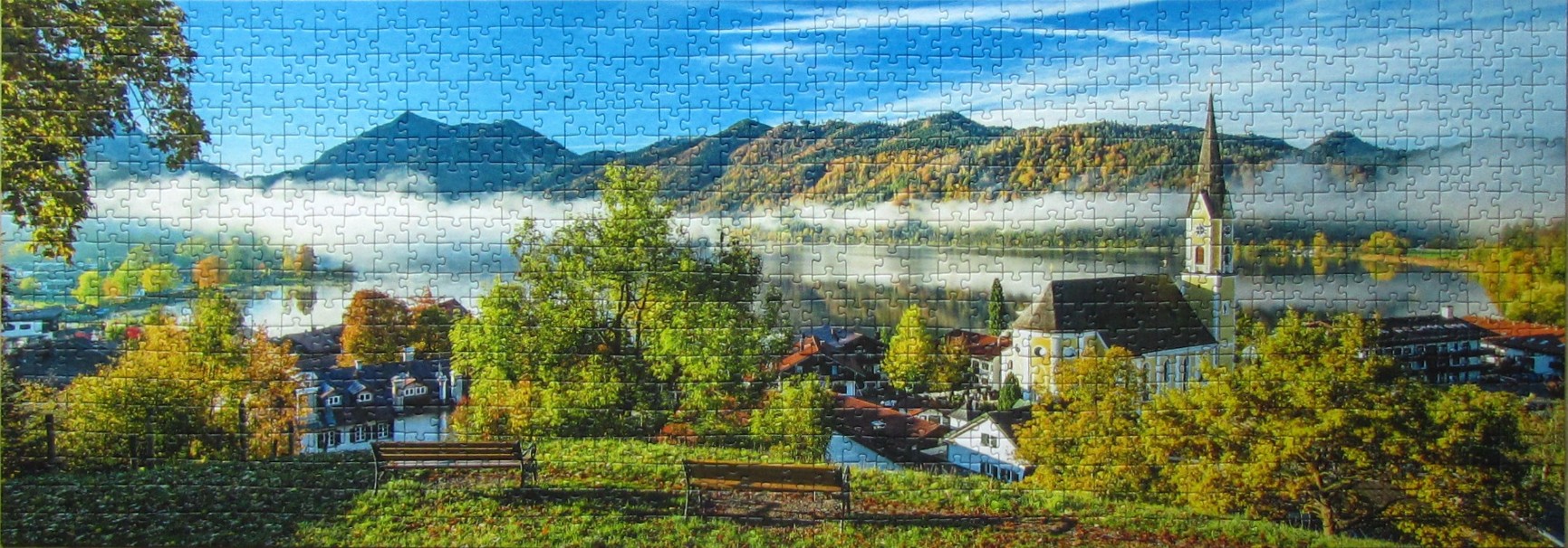 Panoramic view of a Bavarian village with a church and lake surrounded by mountains in autumn.
