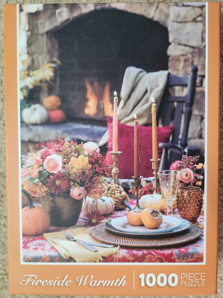 A cozy autumn table setting with a floral centerpiece, pumpkins, and candles in front of a stone fireplace.