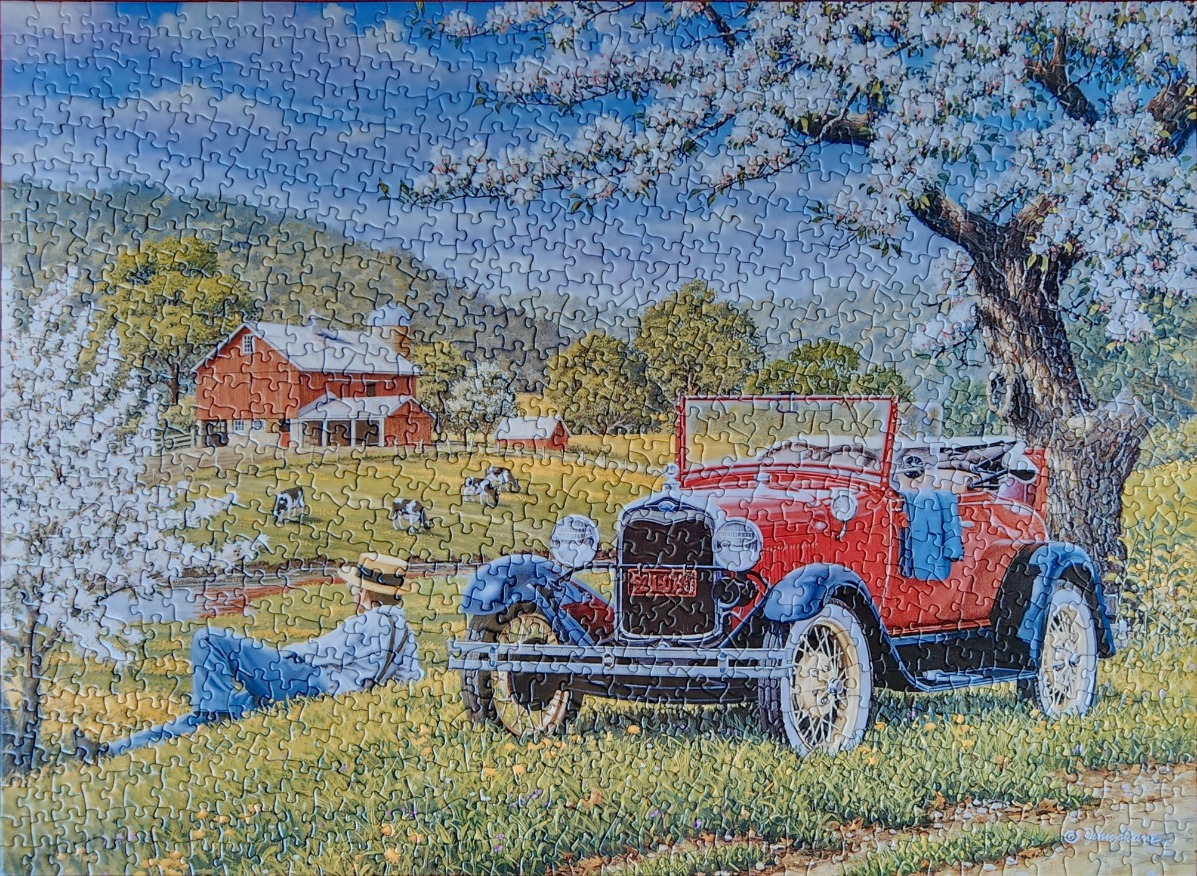 A vintage red car parked under a blooming tree on a farm with a farmer resting in the grass.