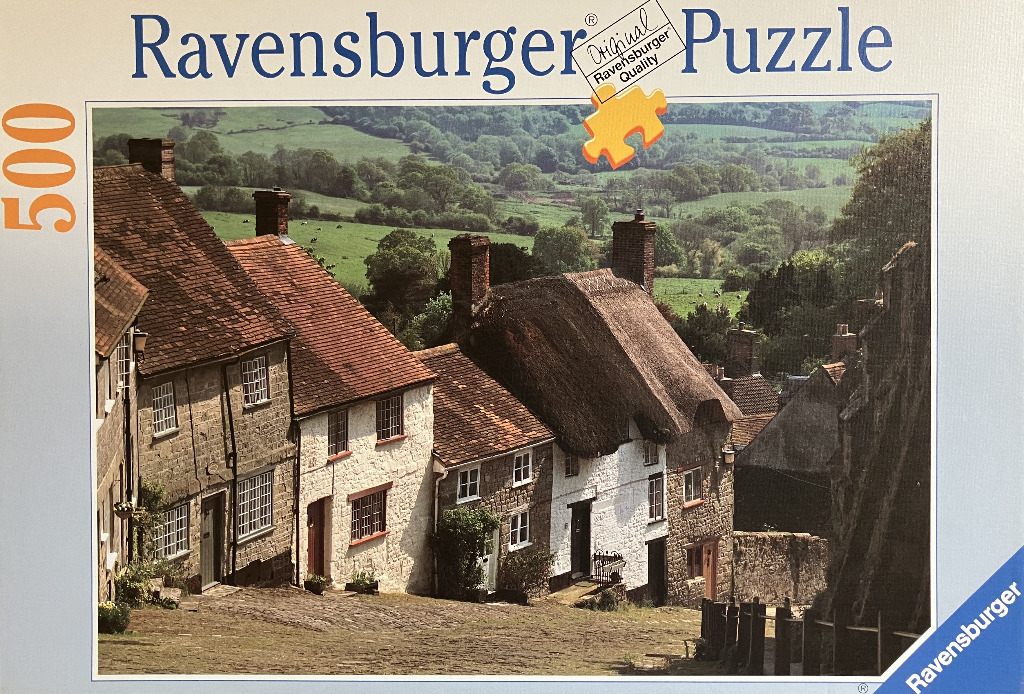 A row of historic English cottages on a hillside overlooking a lush green valley.