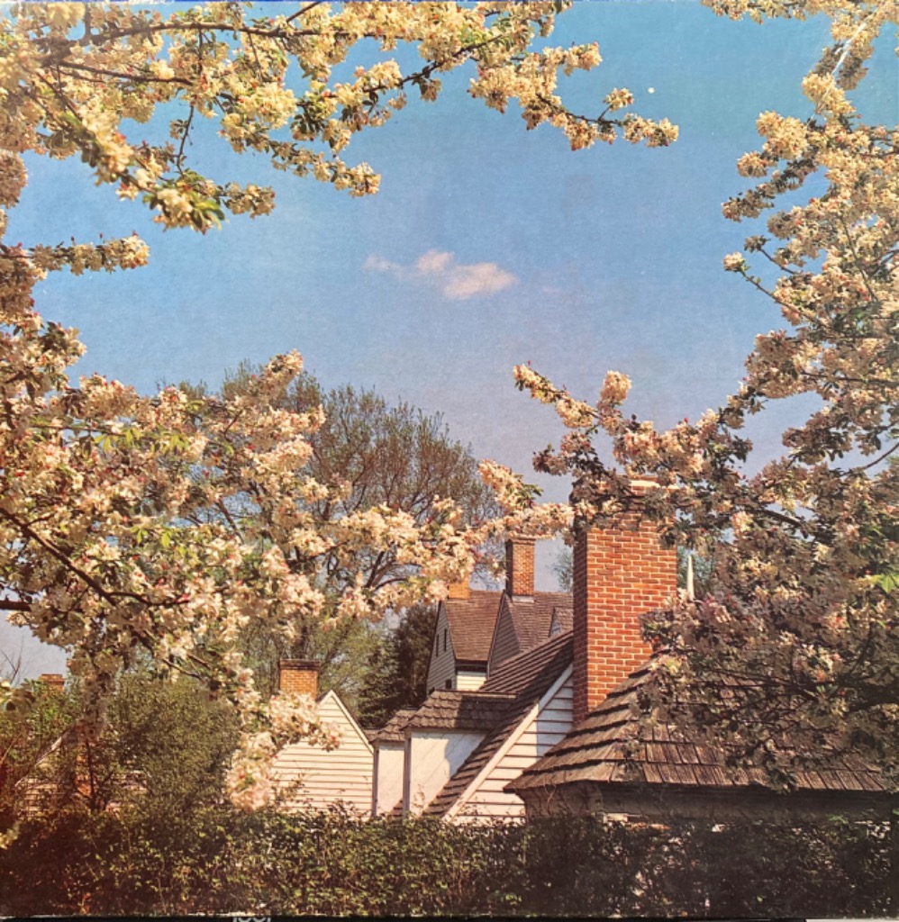 A sunny spring scene with white blossoms framing a red-brick house with wooden shingles against a blue sky.