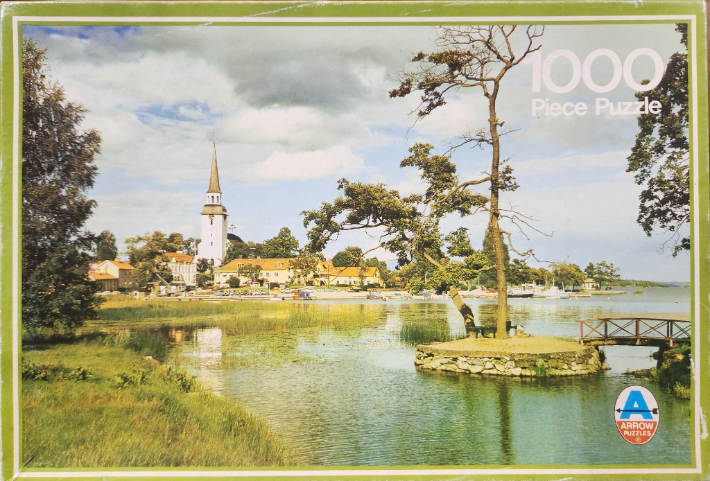 A peaceful Swedish-style lakeside village with a tall church spire and a small, tree-covered island in the foreground.