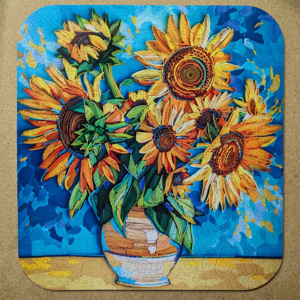 A paper quilling art piece featuring a vibrant bouquet of sunflowers in a vase against a blue background.