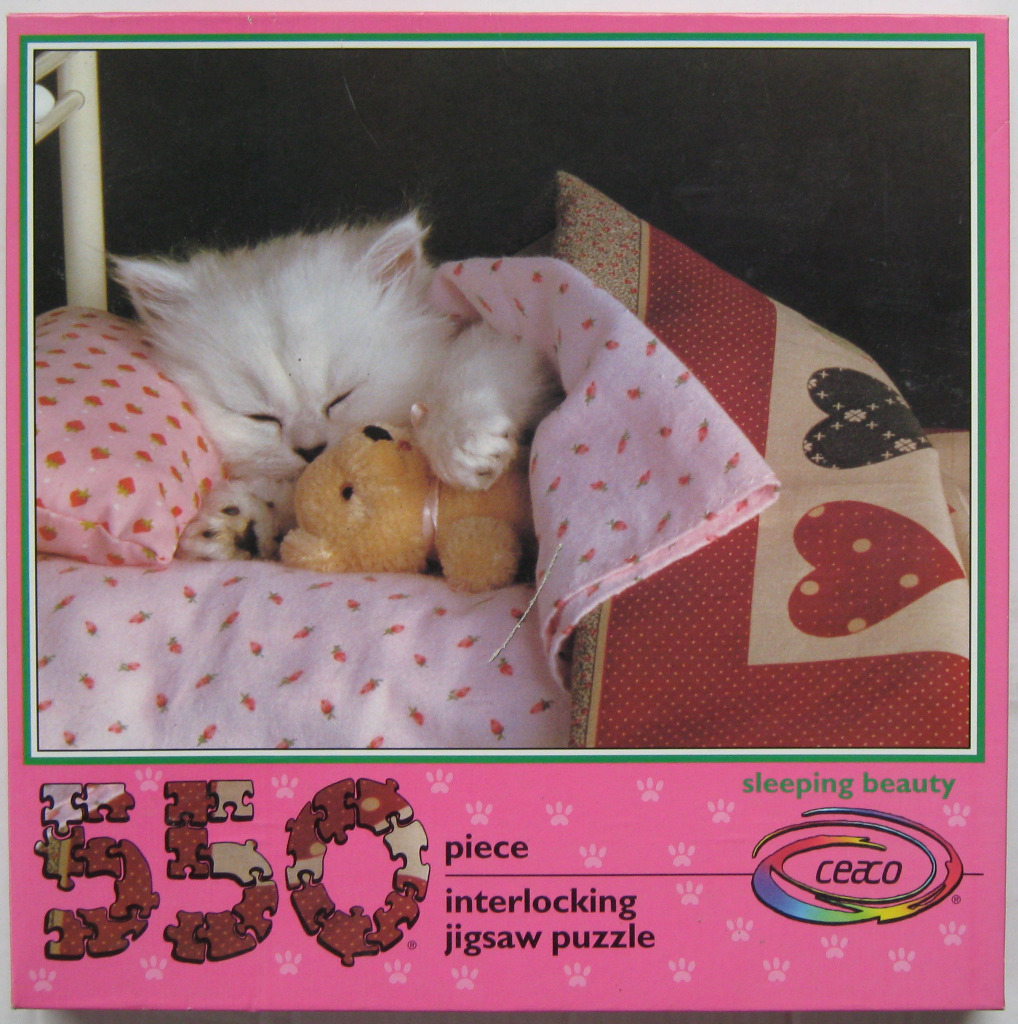 A white fluffy kitten sleeping in a bed while hugging a small teddy bear.
