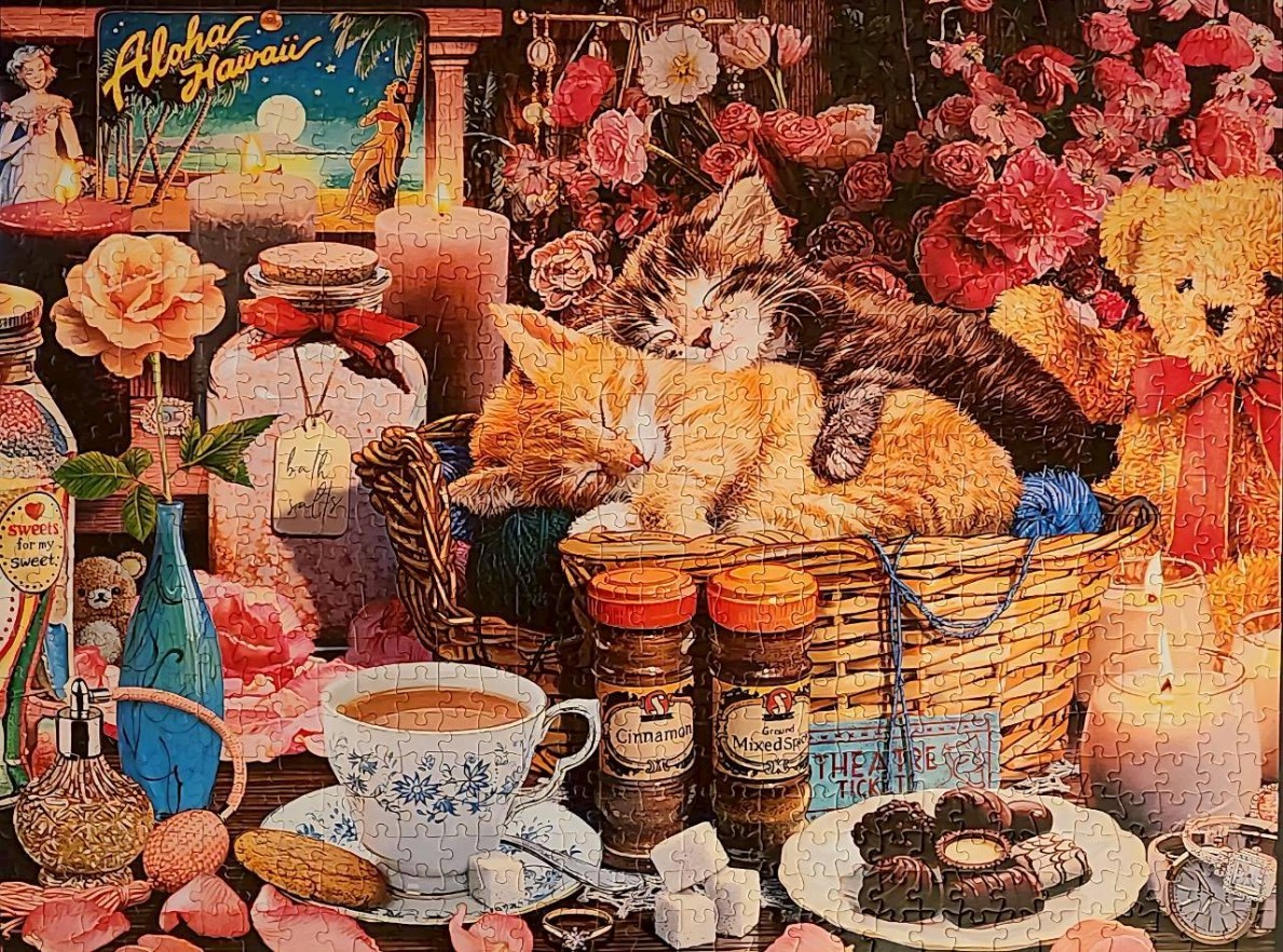 Two kittens sleeping in a wicker basket surrounded by cozy home decor, candles, and flowers.