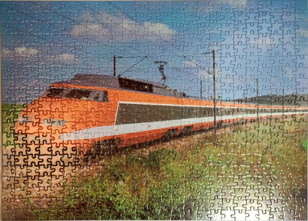 An orange and white high-speed train traveling through a grassy landscape under a blue sky.