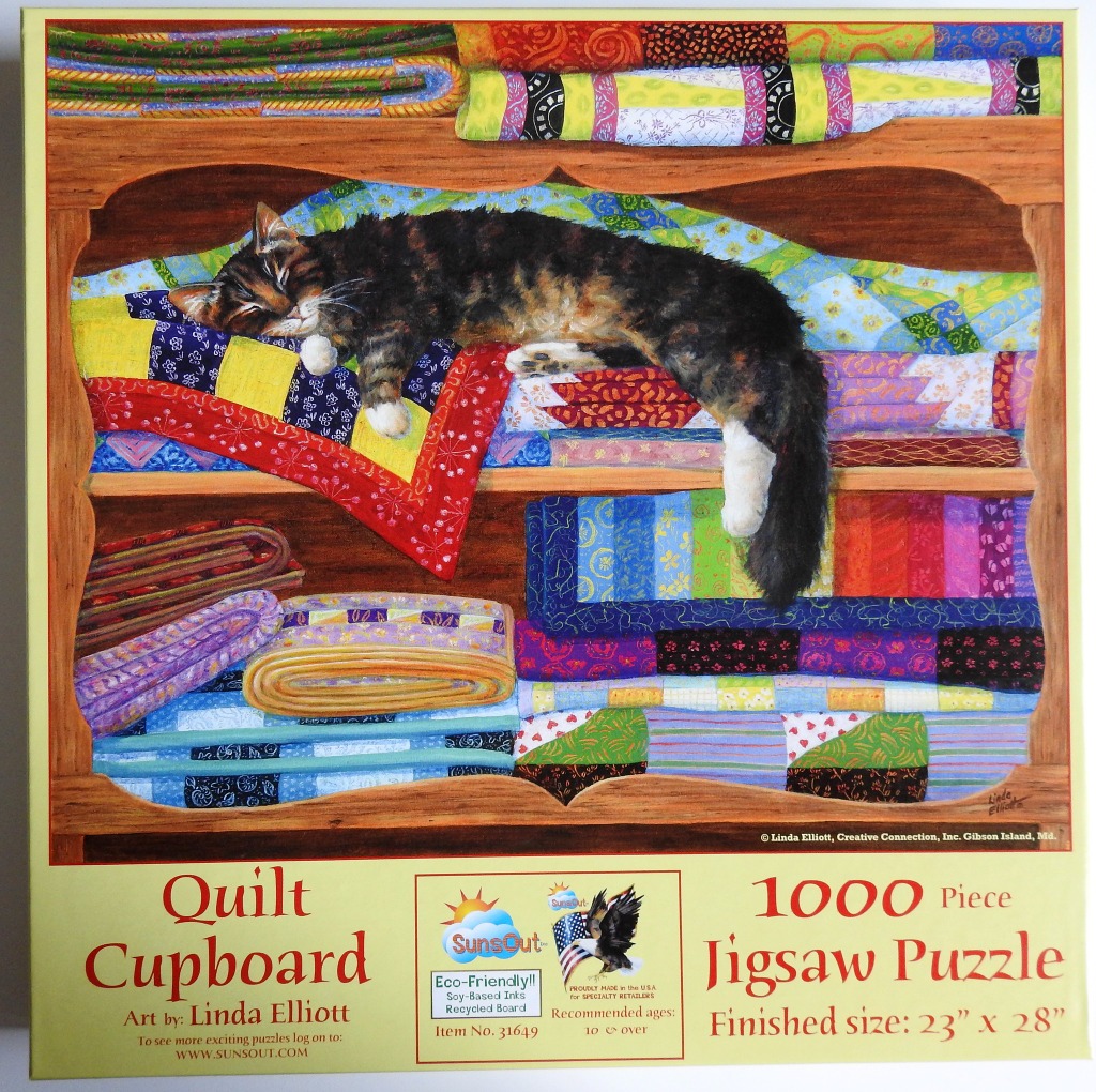 A tortoiseshell cat sleeping on a stack of colorful fabric quilts inside a wooden cupboard.