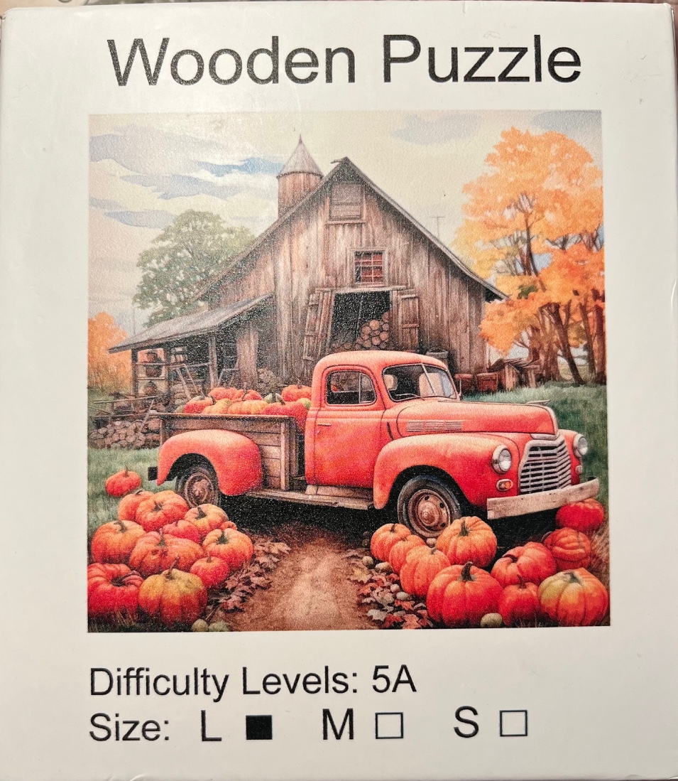 A vintage red pickup truck filled with pumpkins parked in front of a rustic wooden barn in autumn.