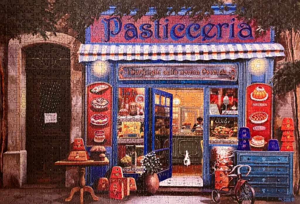 A warm, inviting Italian pastry shop storefront at twilight with a blue facade, pastries in the window, and a tricycle.