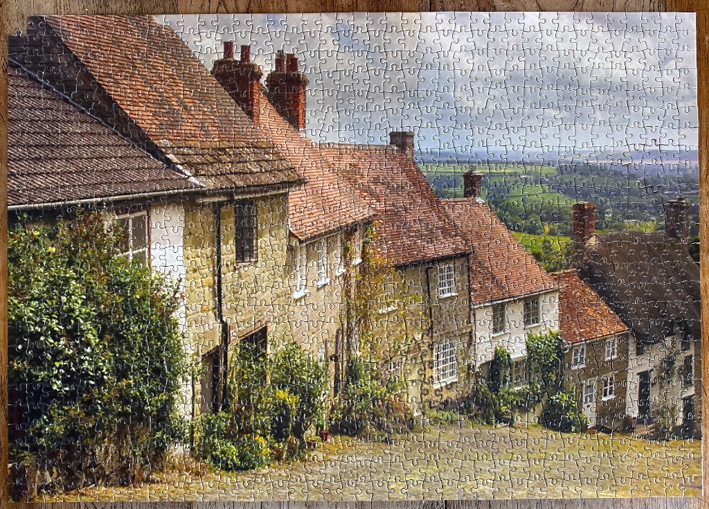 A row of rustic stone cottages on a hillside overlooking a lush green valley under a cloudy sky.