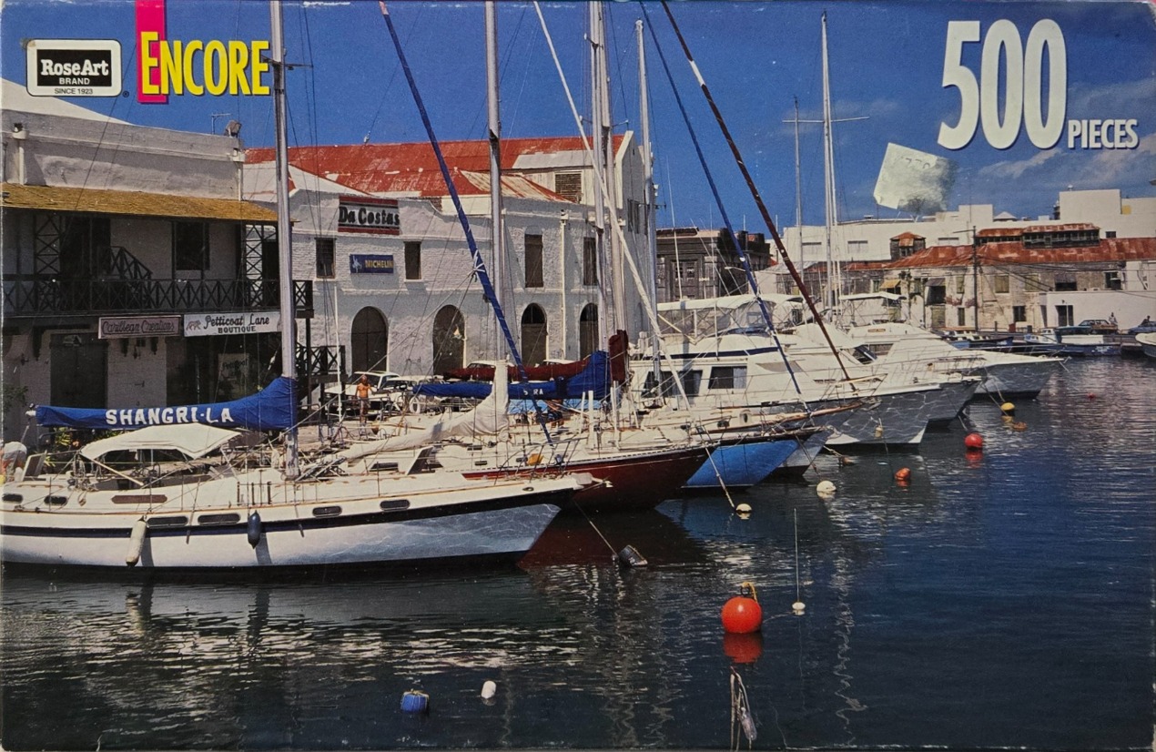 A sunny harbour scene featuring docked sailboats and white buildings along a waterfront.