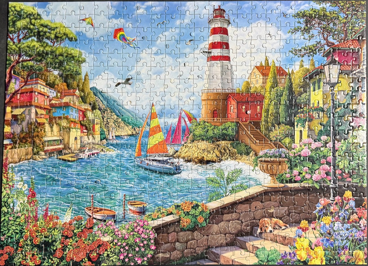 A sunny Mediterranean coastal village scene with a lighthouse, sailboats, and colorful flower gardens.