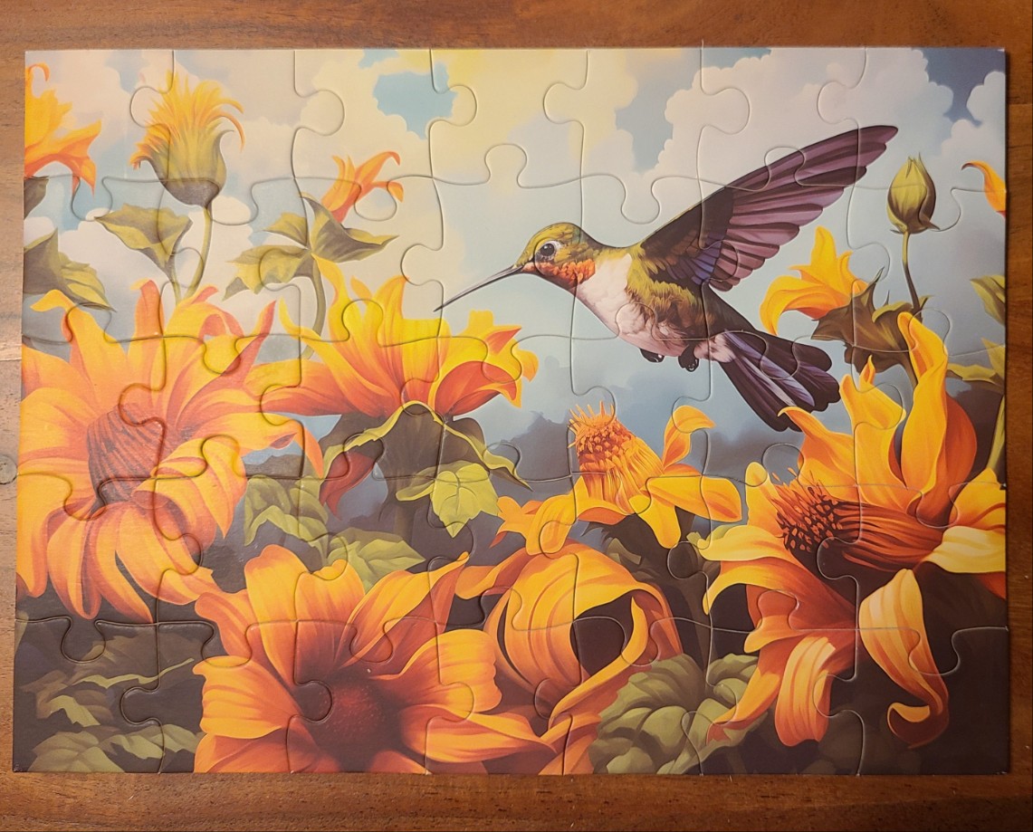 A hummingbird flying among bright yellow sunflowers against a light blue sky.