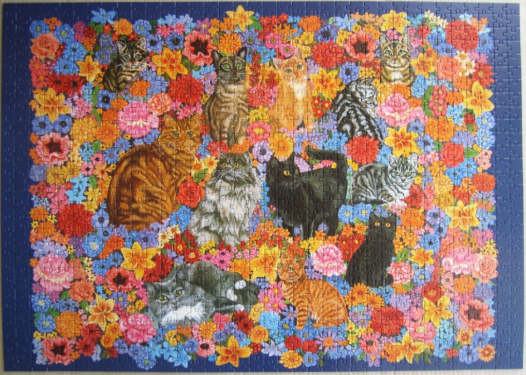 Twelve different cats nestled among a vibrant, colourful garden of mixed flowers.