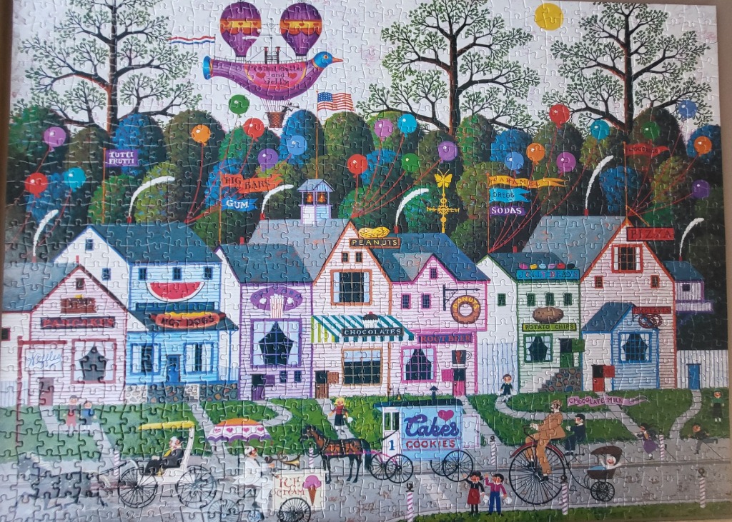 Whimsical illustration of a small town street filled with shops selling various treats and colorful balloons.
