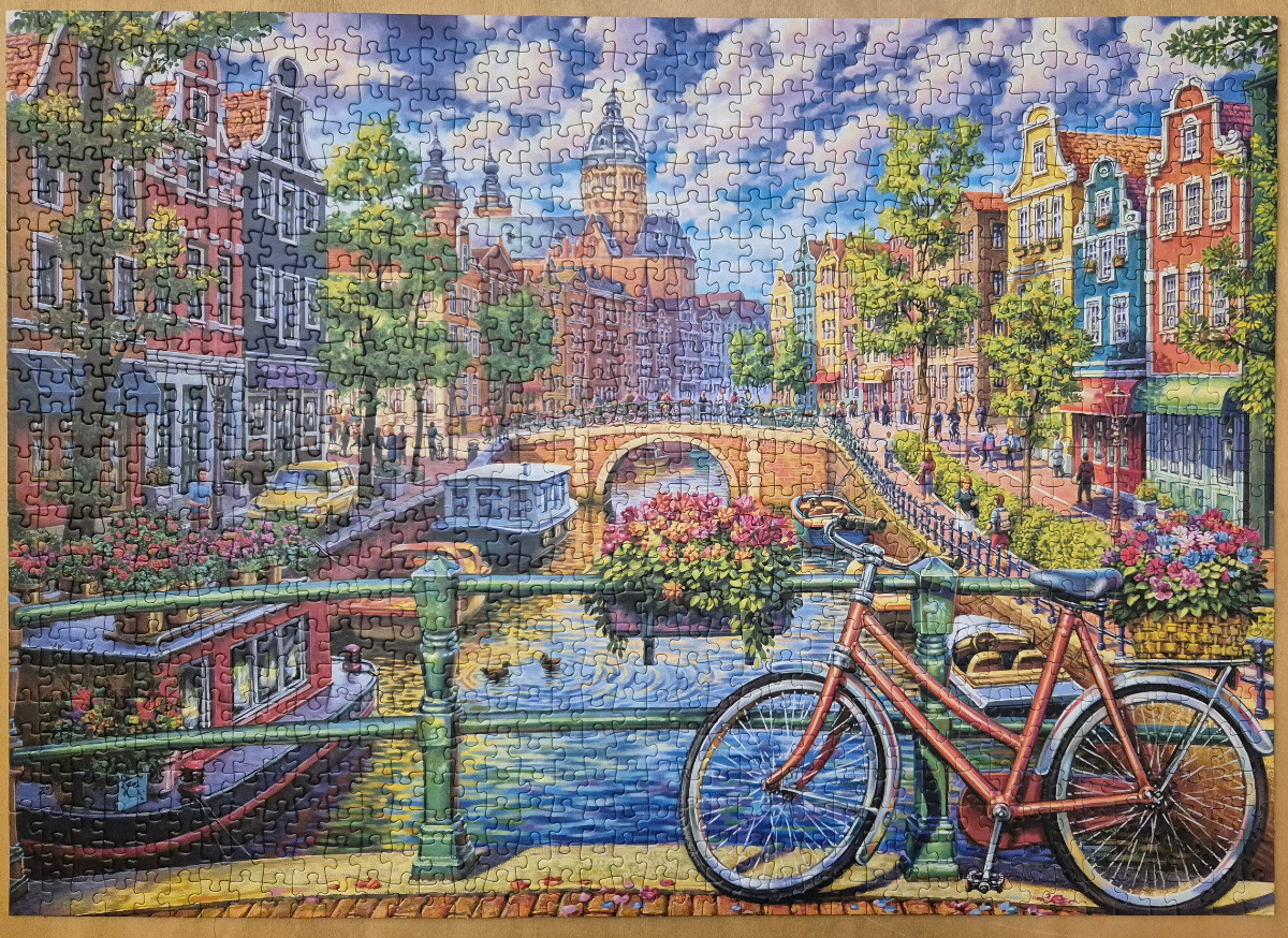 A charming Amsterdam canal scene with a bicycle in the foreground, colourful houses, and a large church in the distance.