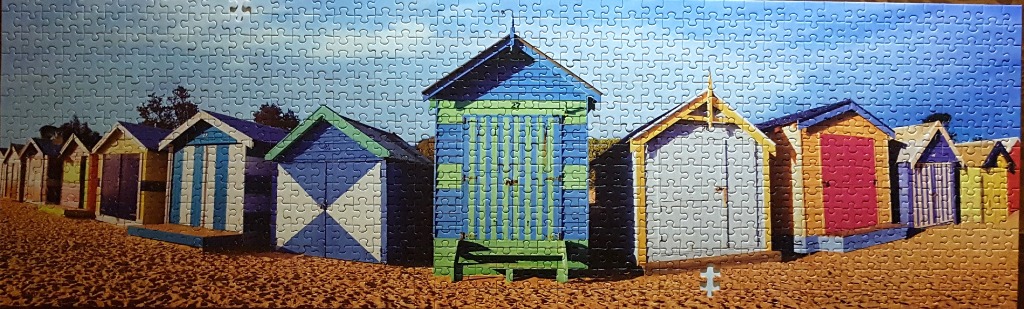 A panoramic view of colourful, vibrant beach huts lined up along a sandy beach under a clear blue sky.