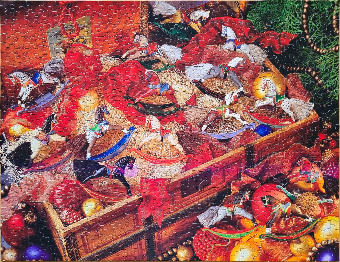 A collection of miniature rocking horse ornaments nested in a wooden crate filled with straw and Christmas decorations.