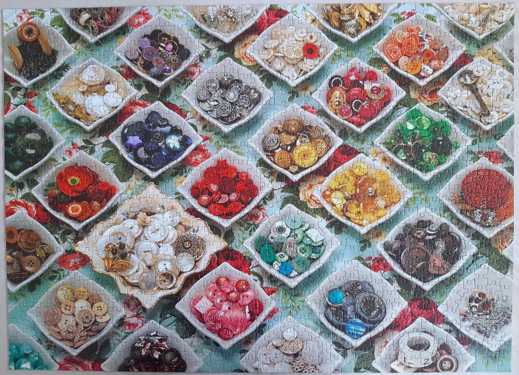 Collection of small square bowls filled with colorful vintage buttons and sewing supplies on a floral background.