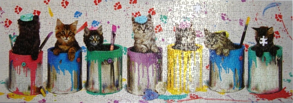 Seven kittens sitting in vibrant, paint-covered metal cans against a white background with splattered paw prints.