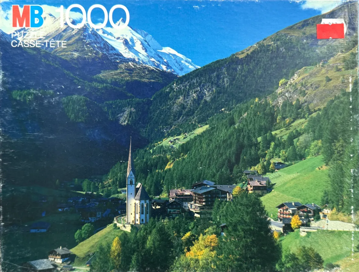 Alpine village nestled in a lush green valley with a snow-capped mountain backdrop.