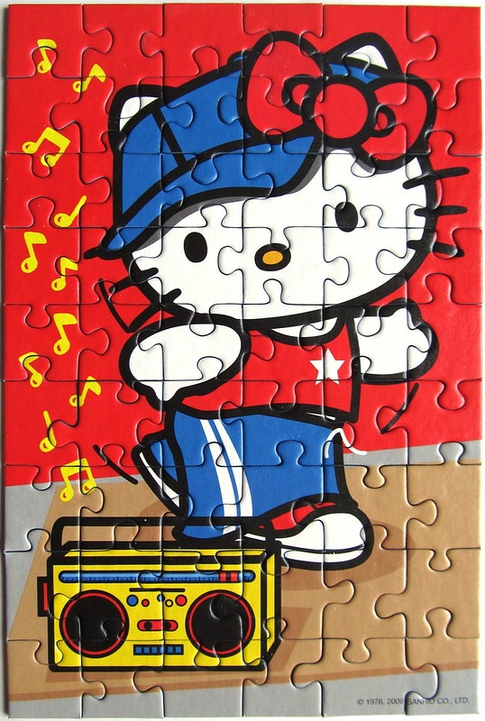 A cartoon illustration of Hello Kitty dressed in hip-hop style clothing standing on a yellow boombox.