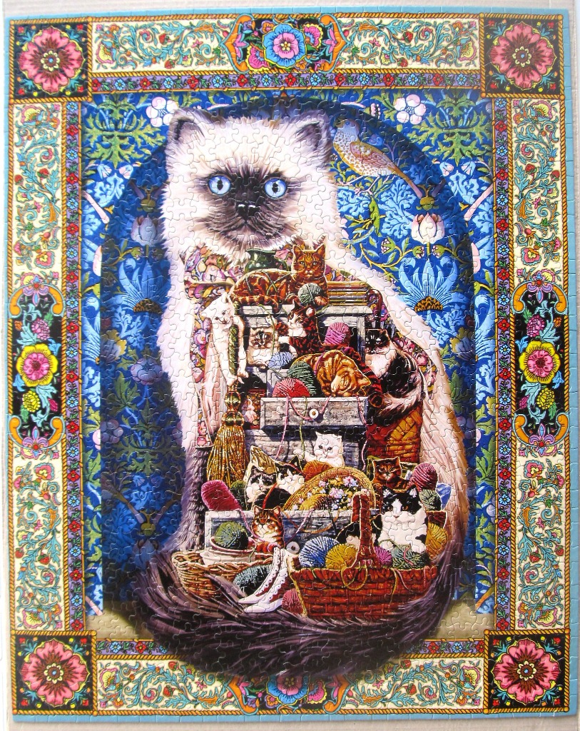 A large, fluffy Ragdoll-style cat sits behind a pile of craft supplies and smaller cats, surrounded by an ornate frame.