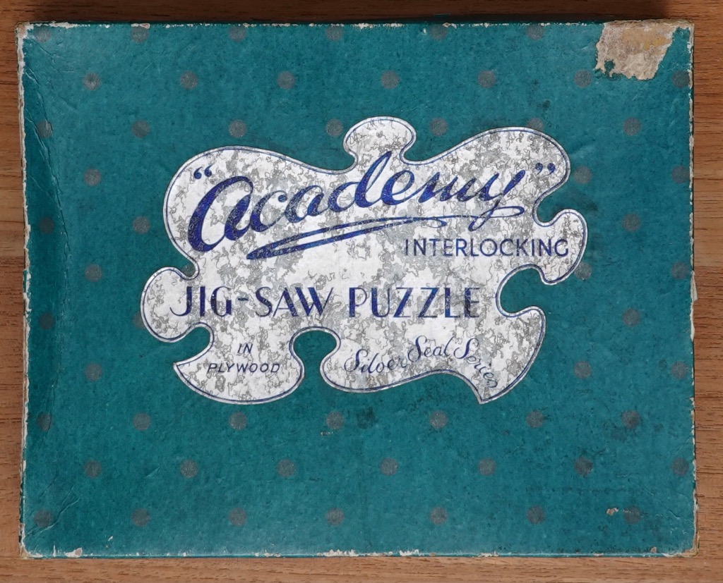 A rectangular teal box with dark polka dots featuring a central silver puzzle-piece shaped label with text.