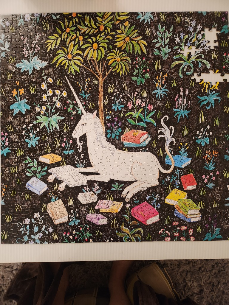 A white unicorn resting under a tree surrounded by colorful books in a botanical tapestry style illustration.