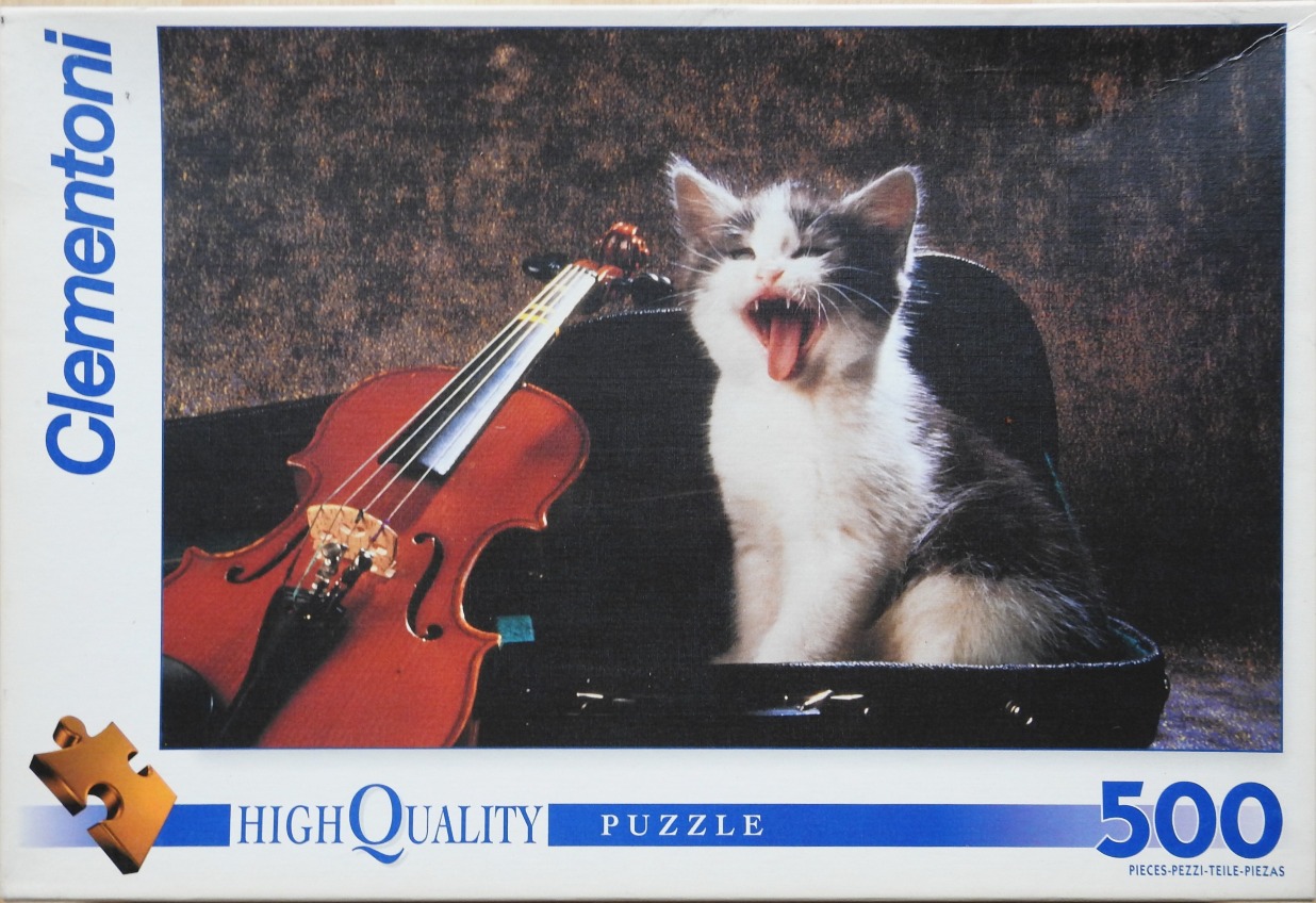 A kitten sits in an open violin case yawning next to a wooden violin against a mottled brown background.