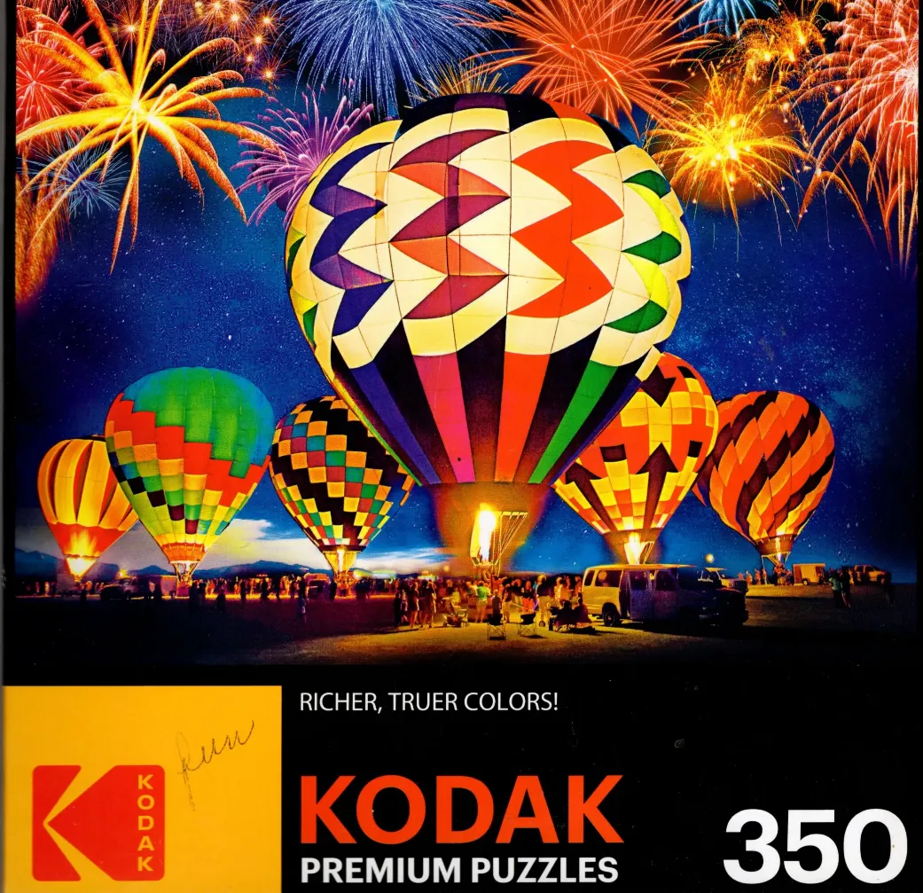 Multiple colorful hot air balloons floating against a dark night sky filled with vibrant fireworks.