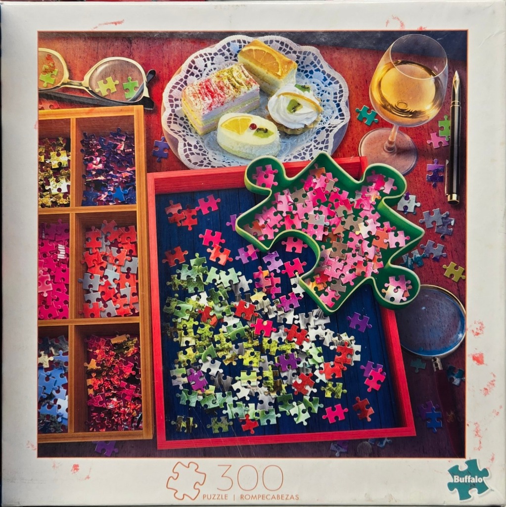 A top-down photograph showing a desktop scene filled with organized jigsaw pieces and snacks.