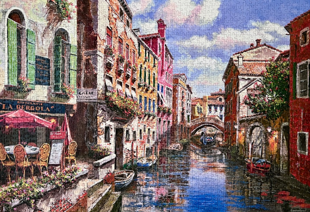 A scenic oil painting of a canal in Venice featuring restaurant seating, aged buildings, and a stone bridge.