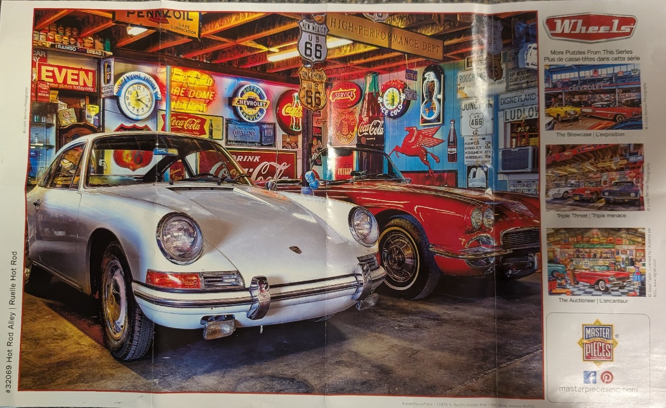 A silver vintage sports car and a red convertible parked inside a garage filled with colorful automotive memorabilia.