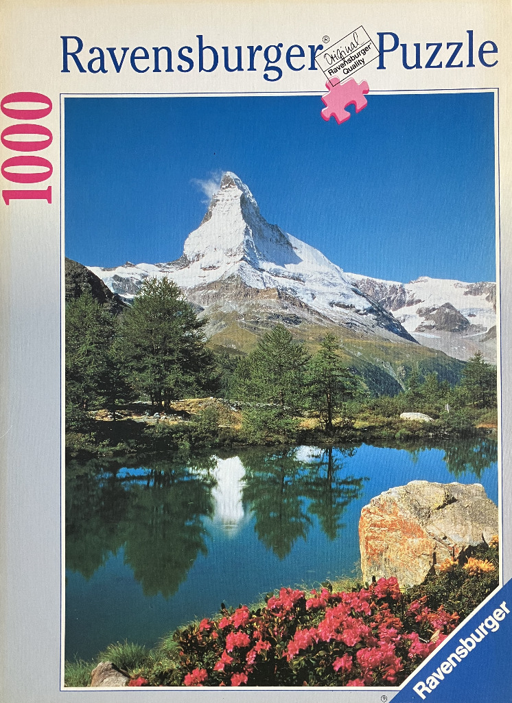 The Matterhorn mountain reflected in a clear alpine lake with pink rhododendrons in the foreground.