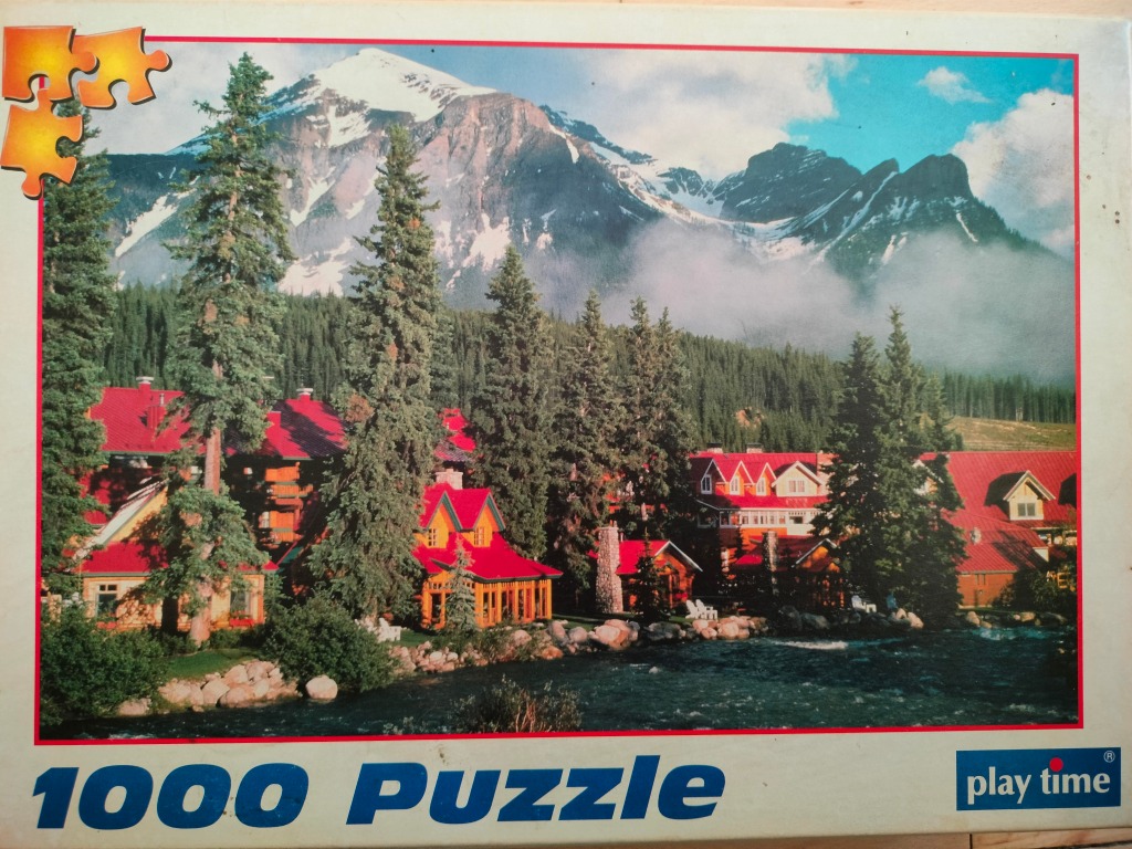 A mountain resort with red-roofed cabins nestled beside a river in front of a snow-capped peak.