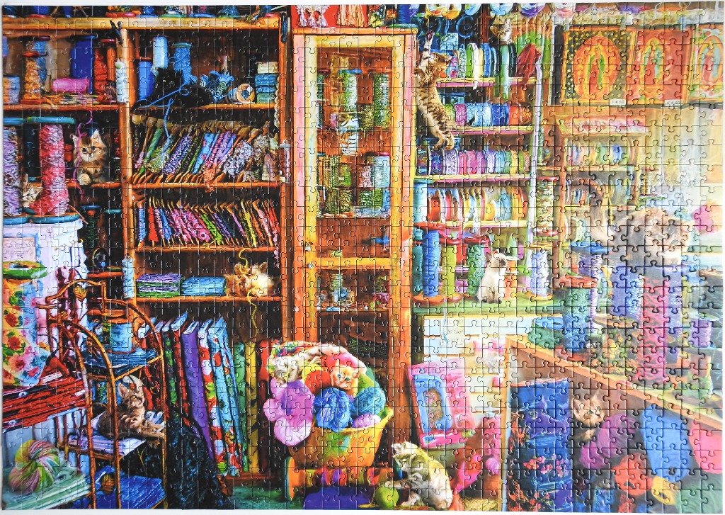 A cozy craft room filled with shelves of yarn, ribbons, fabric, and playful kittens.