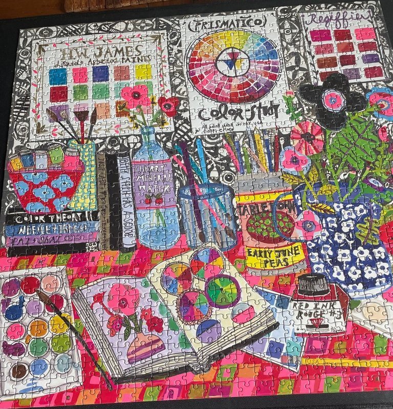 A vibrant, hand-drawn style illustration of a busy artist's studio desk filled with paint supplies and color charts.