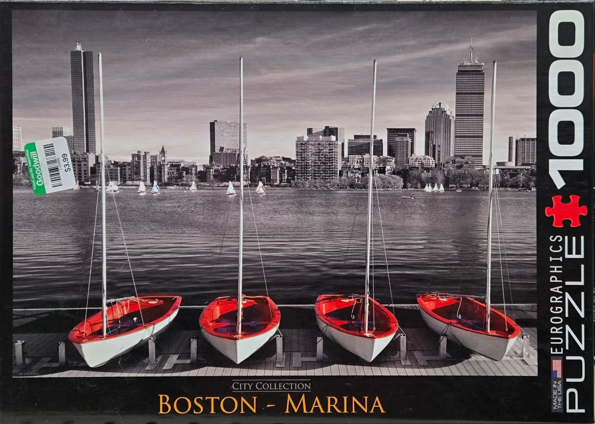 Four bright red sailboats moored at a dock with the black and white Boston skyline in the background.