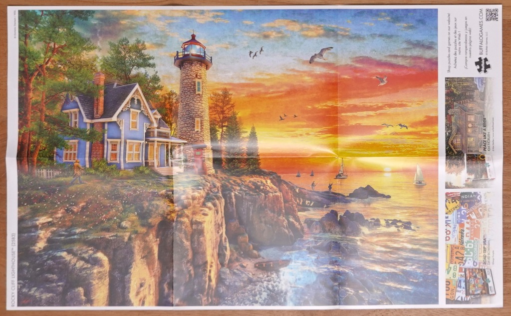 A lighthouse and blue house on a rocky cliff overlooking a sunset over the ocean.