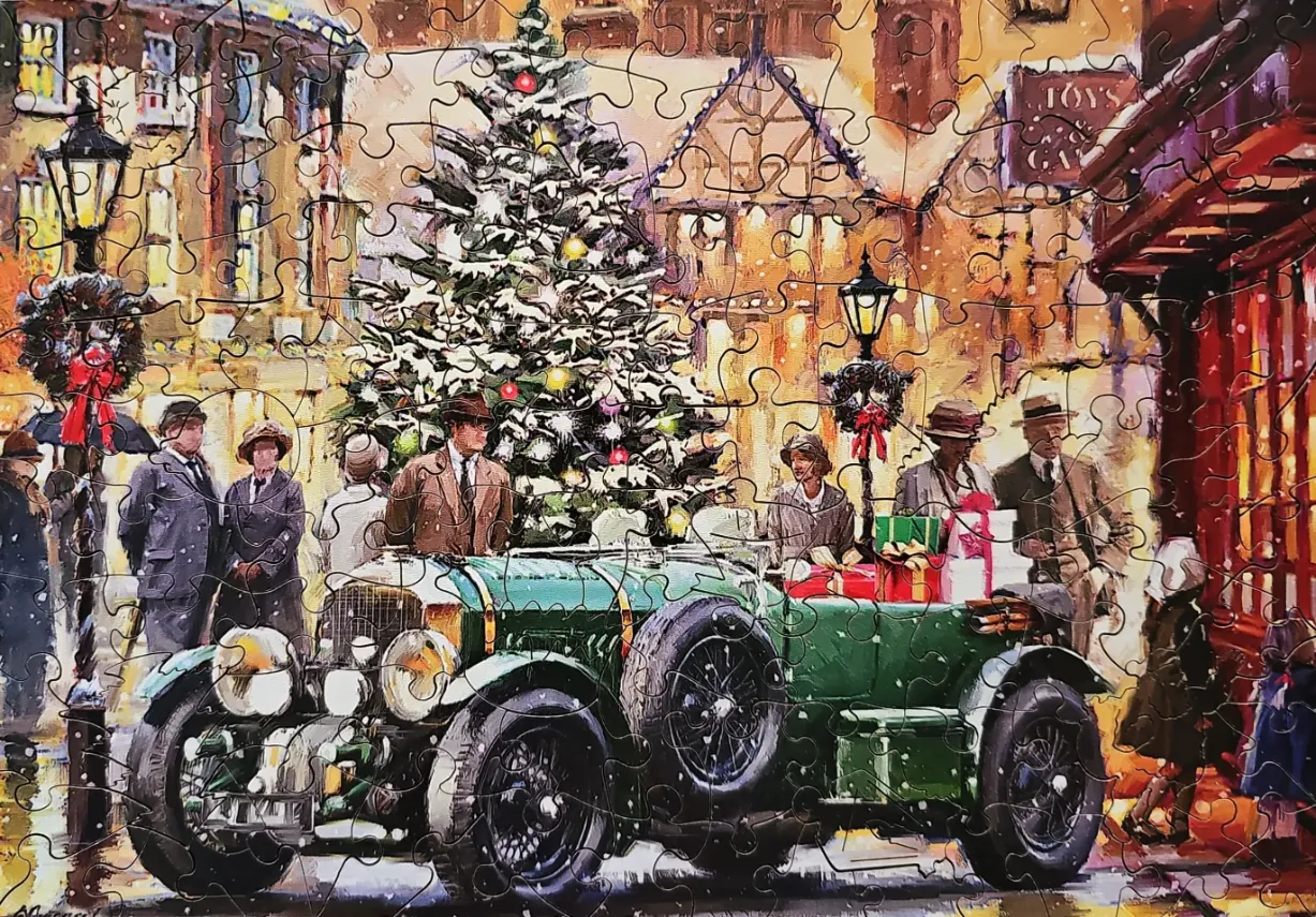 Vintage green car parked in a snowy town square decorated for Christmas, surrounded by people in 1920s attire.