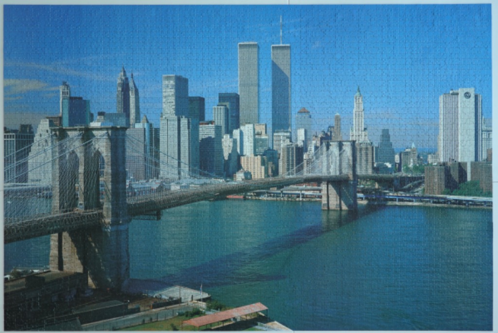 A panoramic view of the New York City skyline featuring the Brooklyn Bridge and the Twin Towers of the World Trade Center.