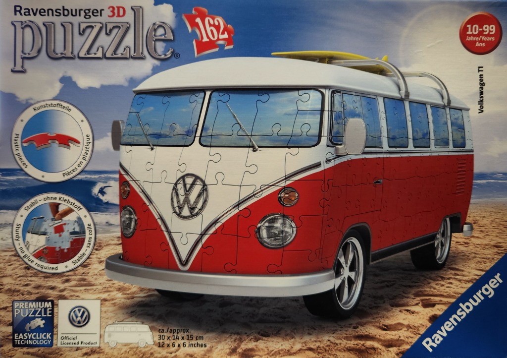 A red and white vintage Volkswagen T1 bus parked on a sandy beach under a bright blue sky.