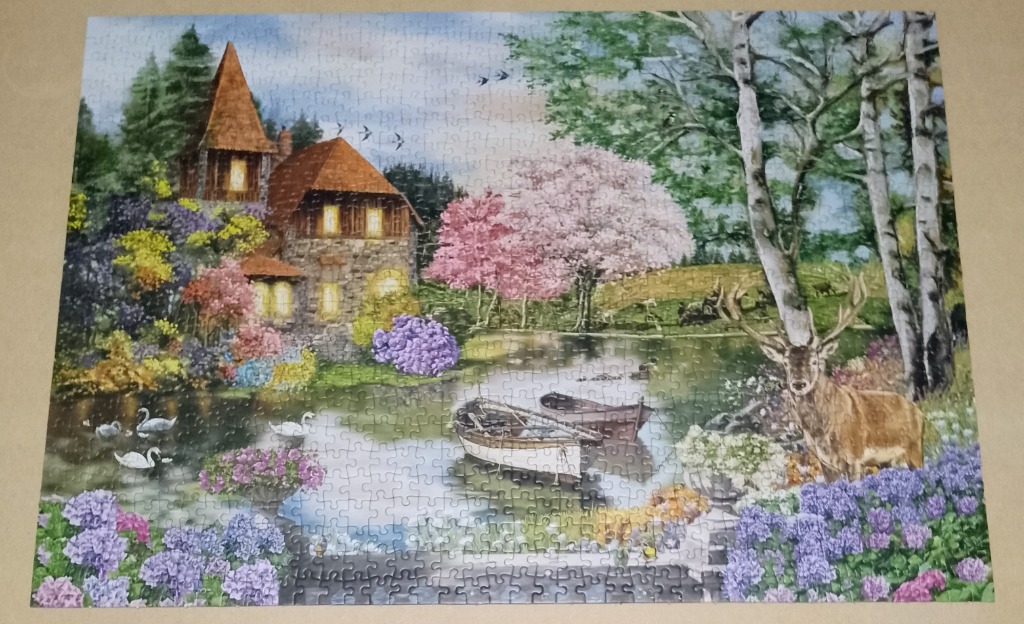 A peaceful stone cottage by a pond with blooming trees, flowers, and a deer in the foreground.