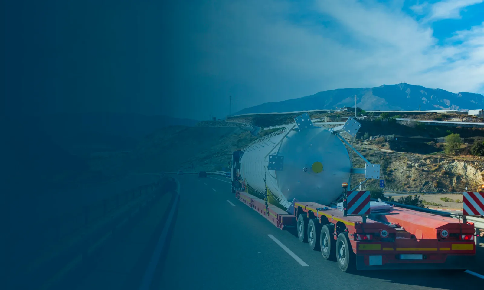 Gigantesco serbatoio bianco su trasporto eccezionale lungo una strada montana sotto un cielo azzurro.