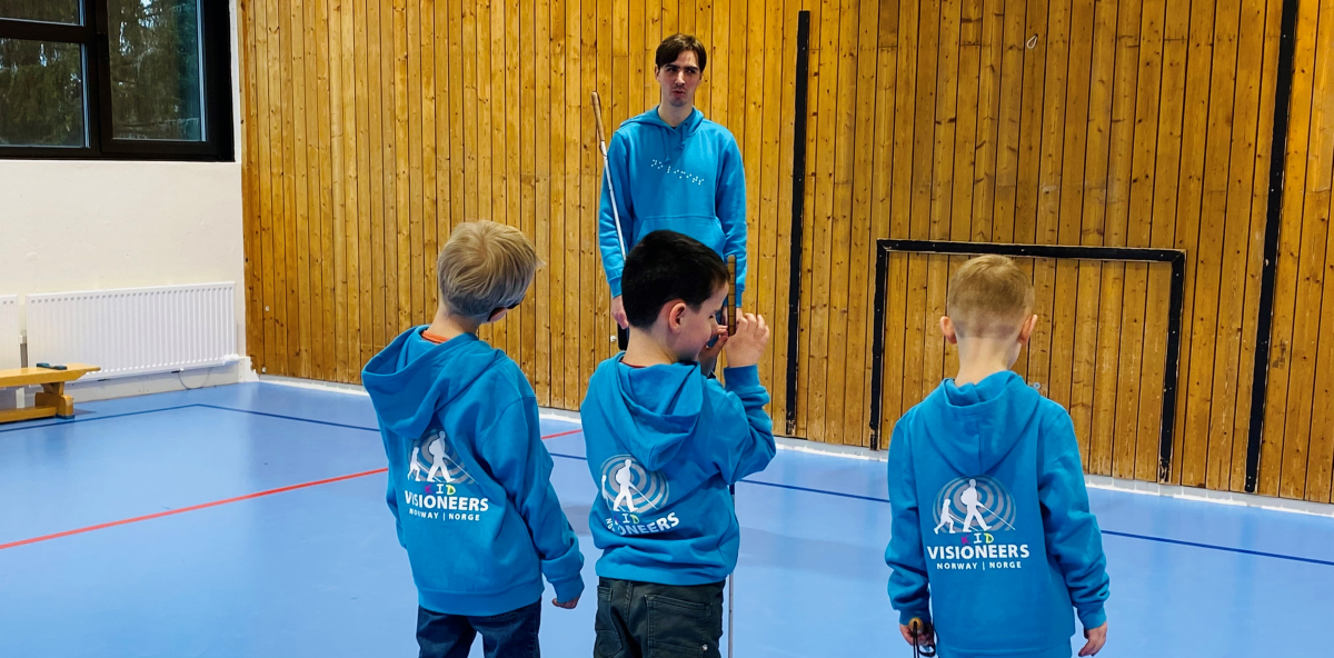 Bildebeskrivelse: Thomas står mot kamera foran tre barn med ryggen til. Alle har Kid Visioneers gensere.