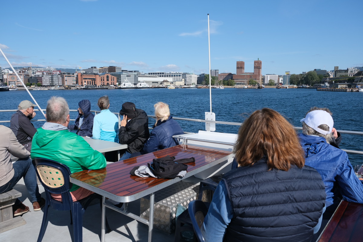 Mennesker sitter rundt et bord på båten og ser ut på fjorden og inn mot Aker Brygge